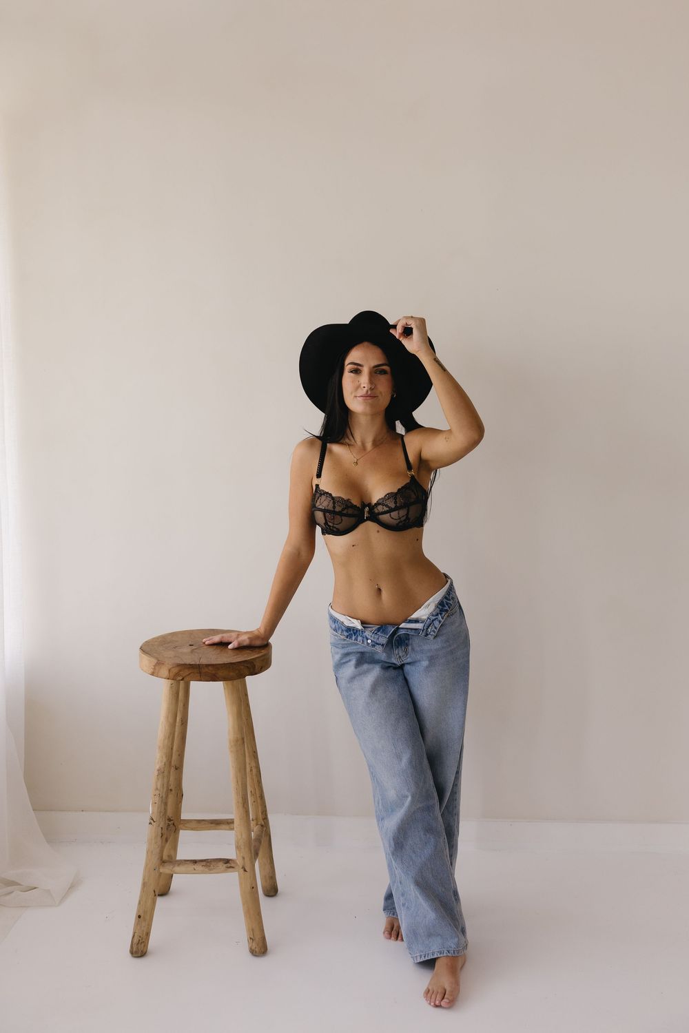 Minimalist photo series featuring a woman in blue jeans and black lingerie posing with a wooden stool against white walls.