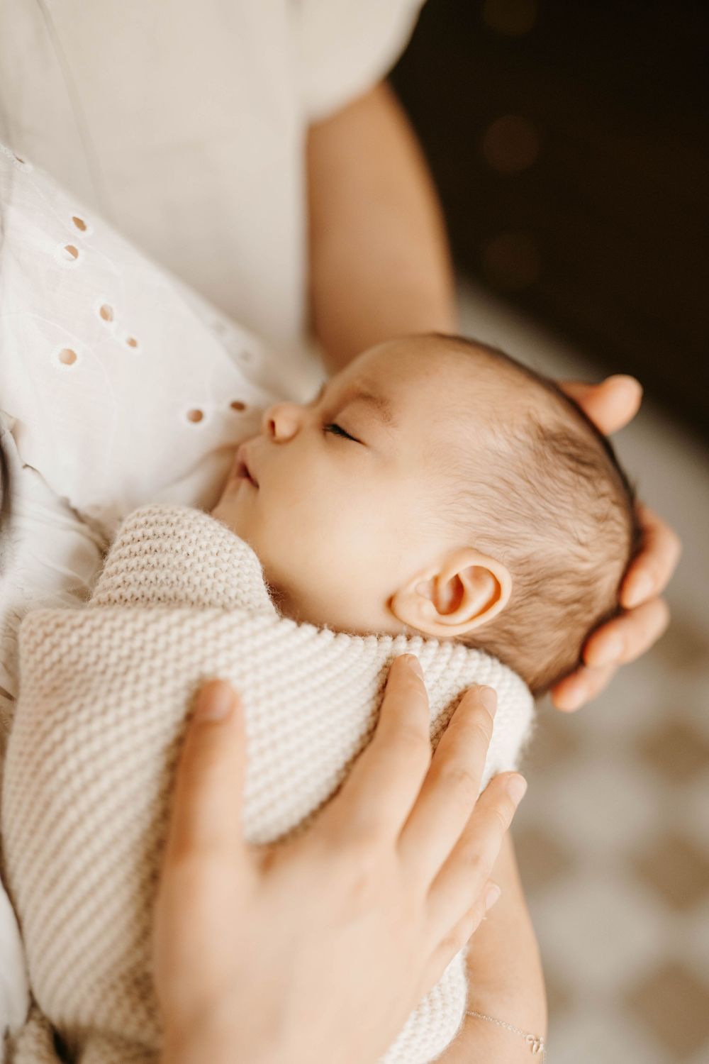 A peaceful newborn baby sleeping soundly while being cradled in a parent's arms, wrapped in a soft knit blanket.
