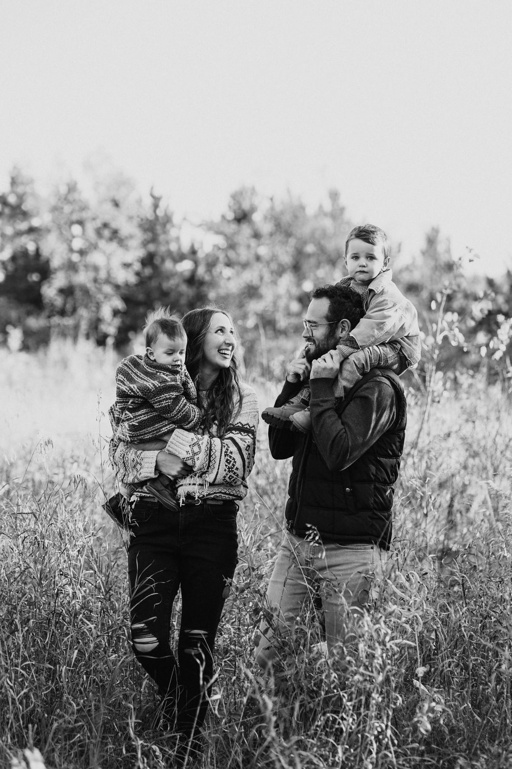 Family enjoying playful moments together in a sunny field during an outdoor photoshoot.
