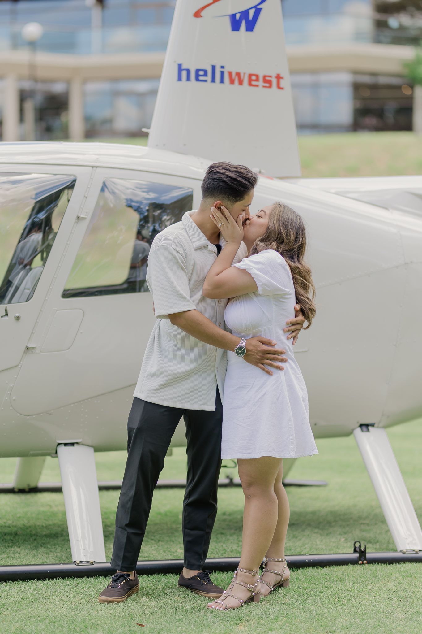 A happy couple in white outfits embrace and laugh together during an outdoor photoshoot.
