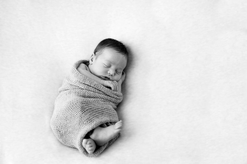 Minimalist black and white newborn photography on white backdrop.