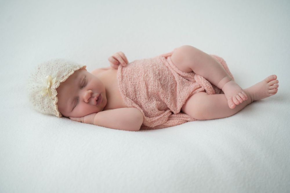 Sleeping infant wearing pink lace outfit and headband on white background.