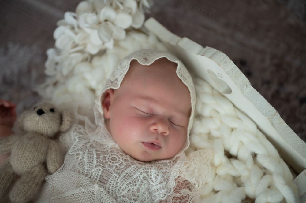 Sleeping newborn in delicate white lace wrap on cream textured blanket.