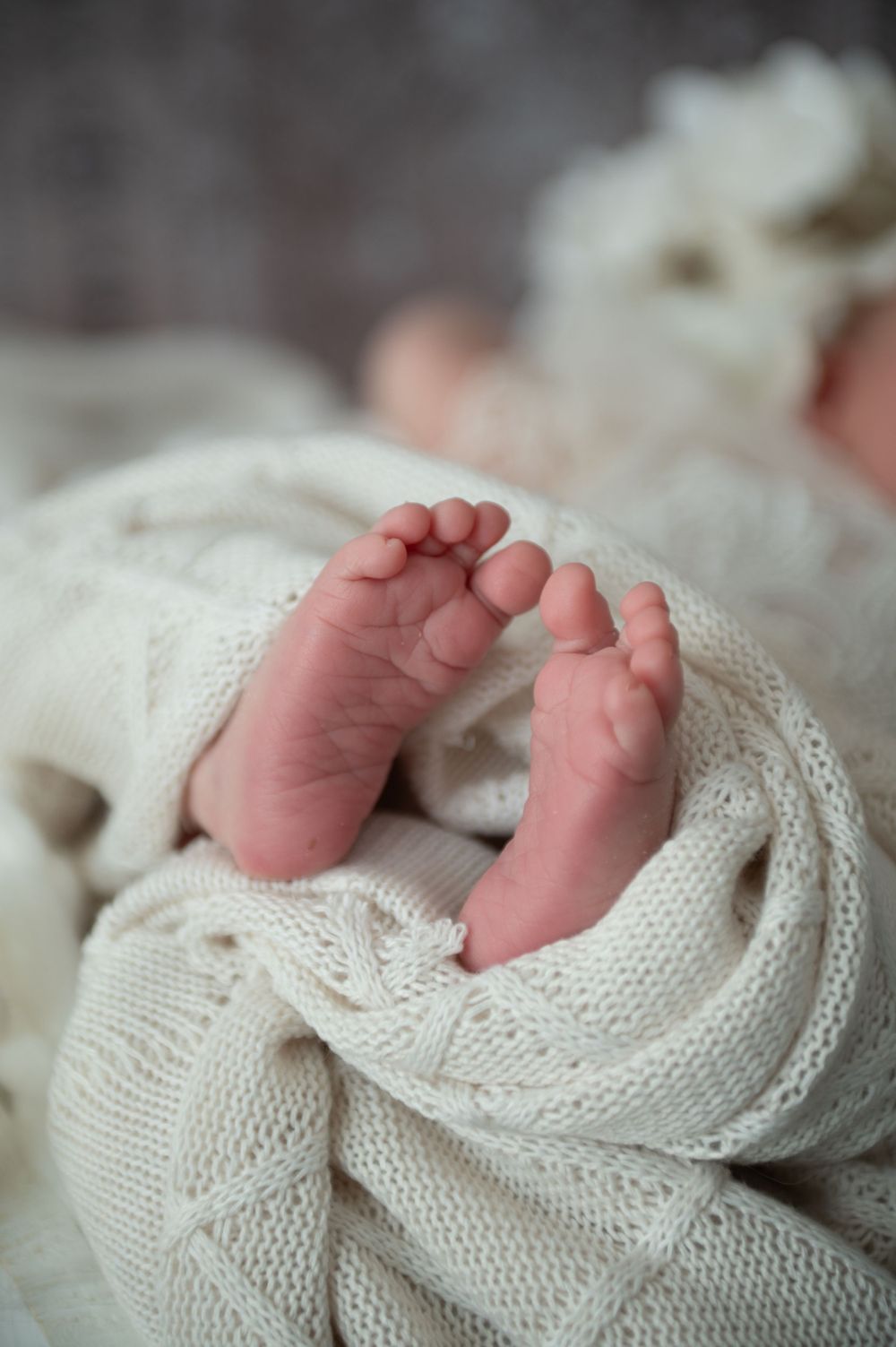 Tiny newborn baby feet resting on soft white knitted blanket in close-up macro shot.
