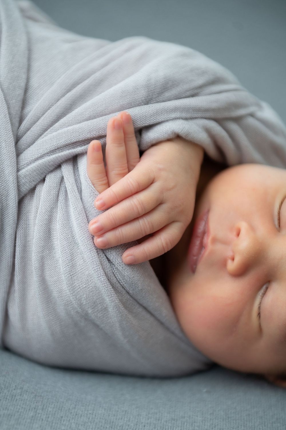 Close up view of sleeping baby swaddled in soft grey fabric.