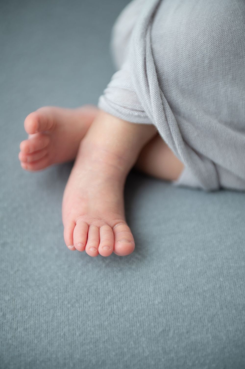 Tiny baby feet and toes peek out from grey wrap against blue background.