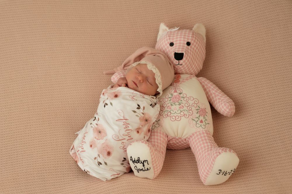 Newborn baby sleeping next to pink teddy bear on beige background.