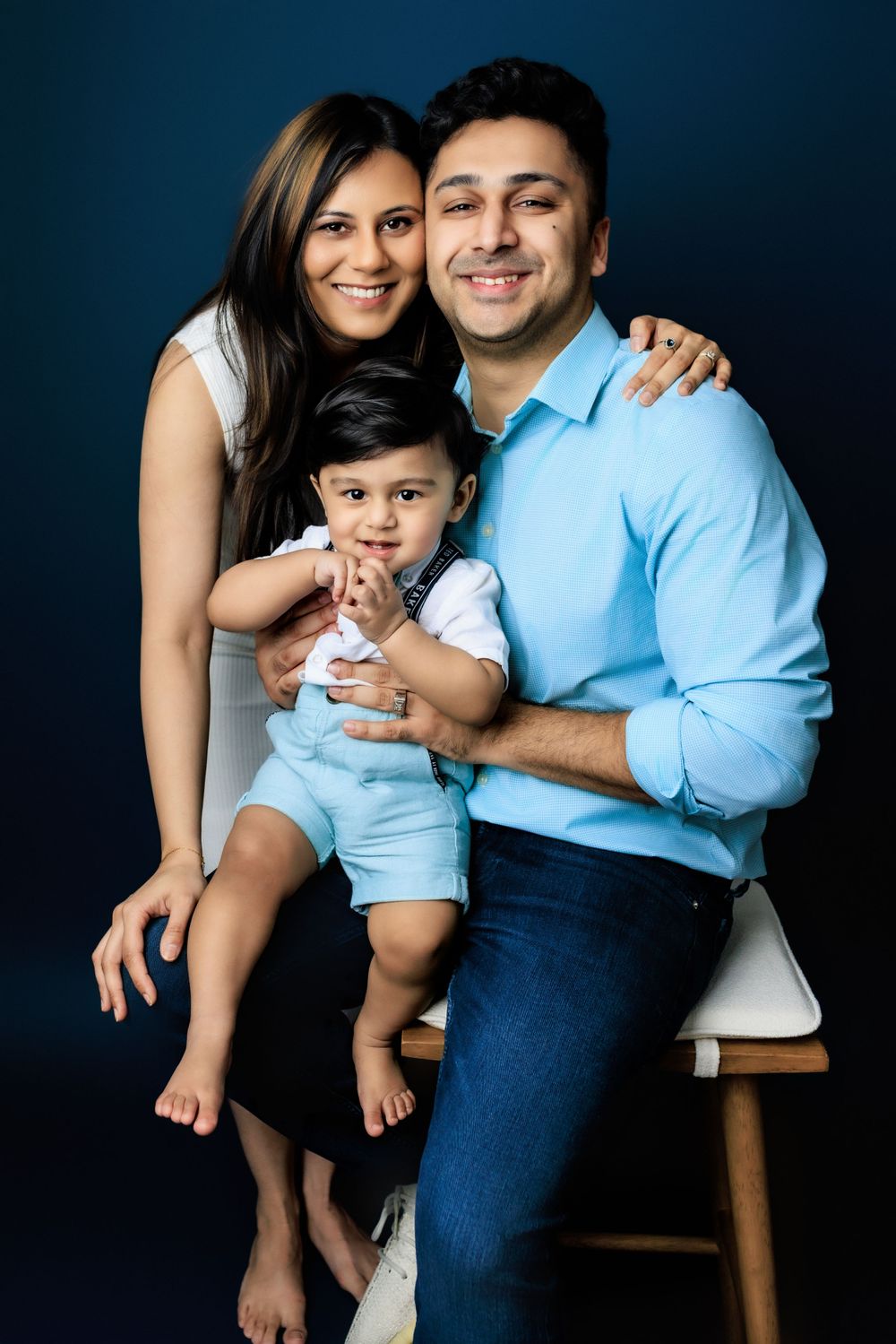 A family in coordinated blue and white outfits poses together against a dark background for a studio portrait.
