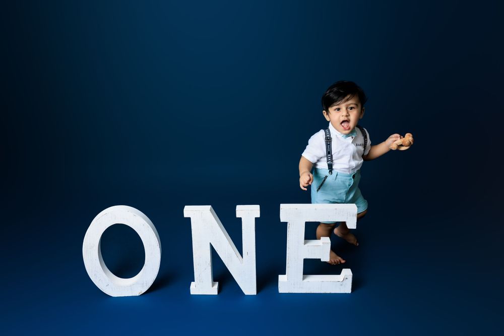 A small child in suspenders stands next to large white letters spelling ONE against a dark blue background.
