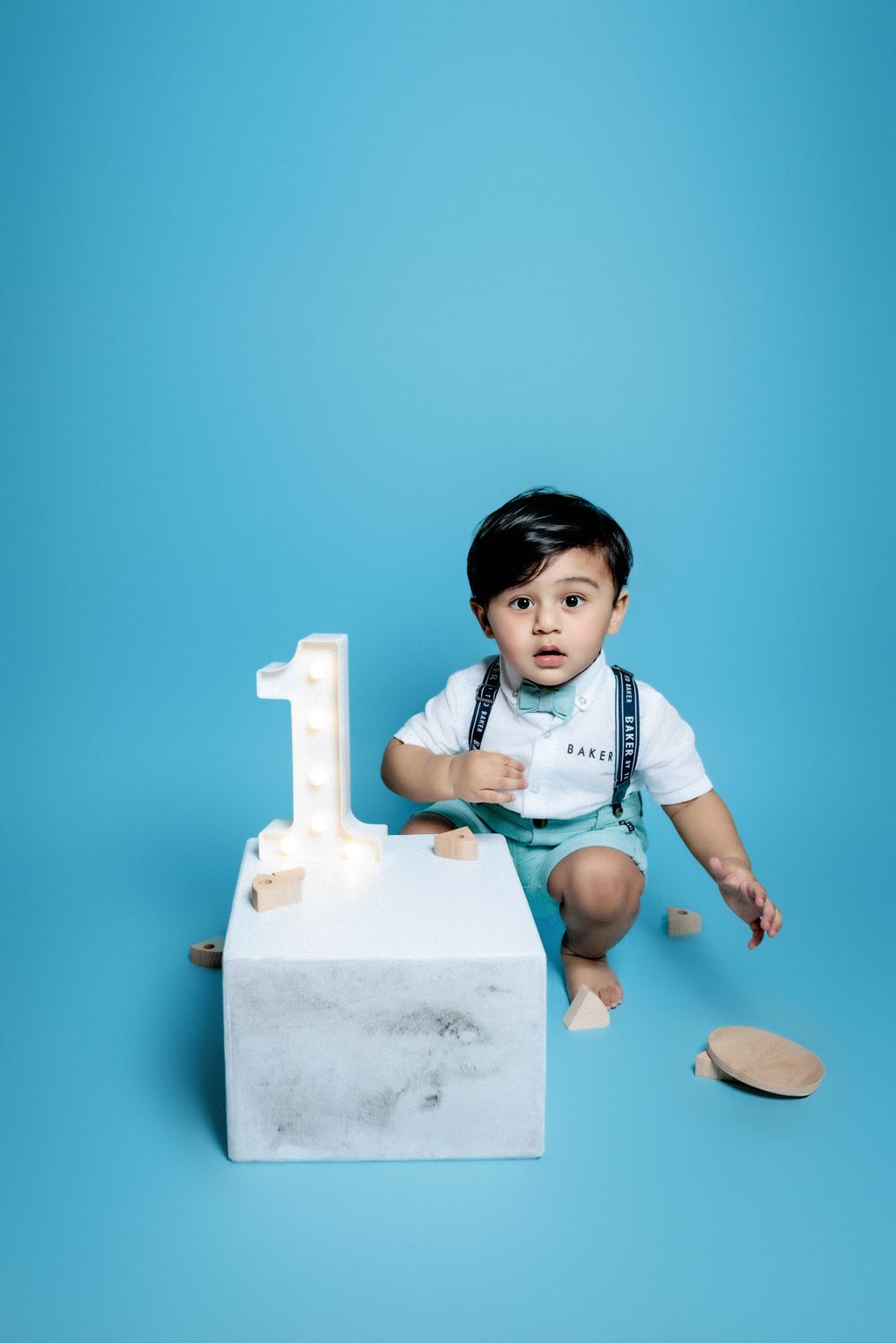 First birthday portrait session with toddler in white shirt and turquoise shorts against bright blue backdrop.