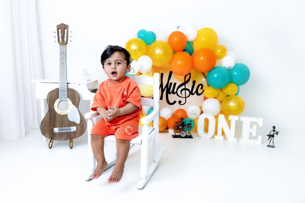 Colorful first birthday party setup with guitar prop and orange and teal balloon decorations on white background.