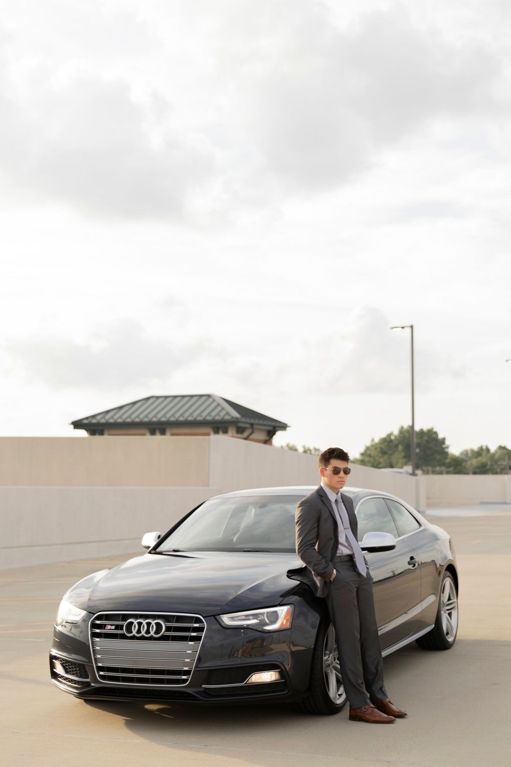 teenage boy posing with his car wearing a suit on the top of a parking garage in rochester