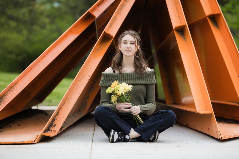 Outdoor senior portrait session with orange architectural structures creating dynamic leading lines and frames in the background.