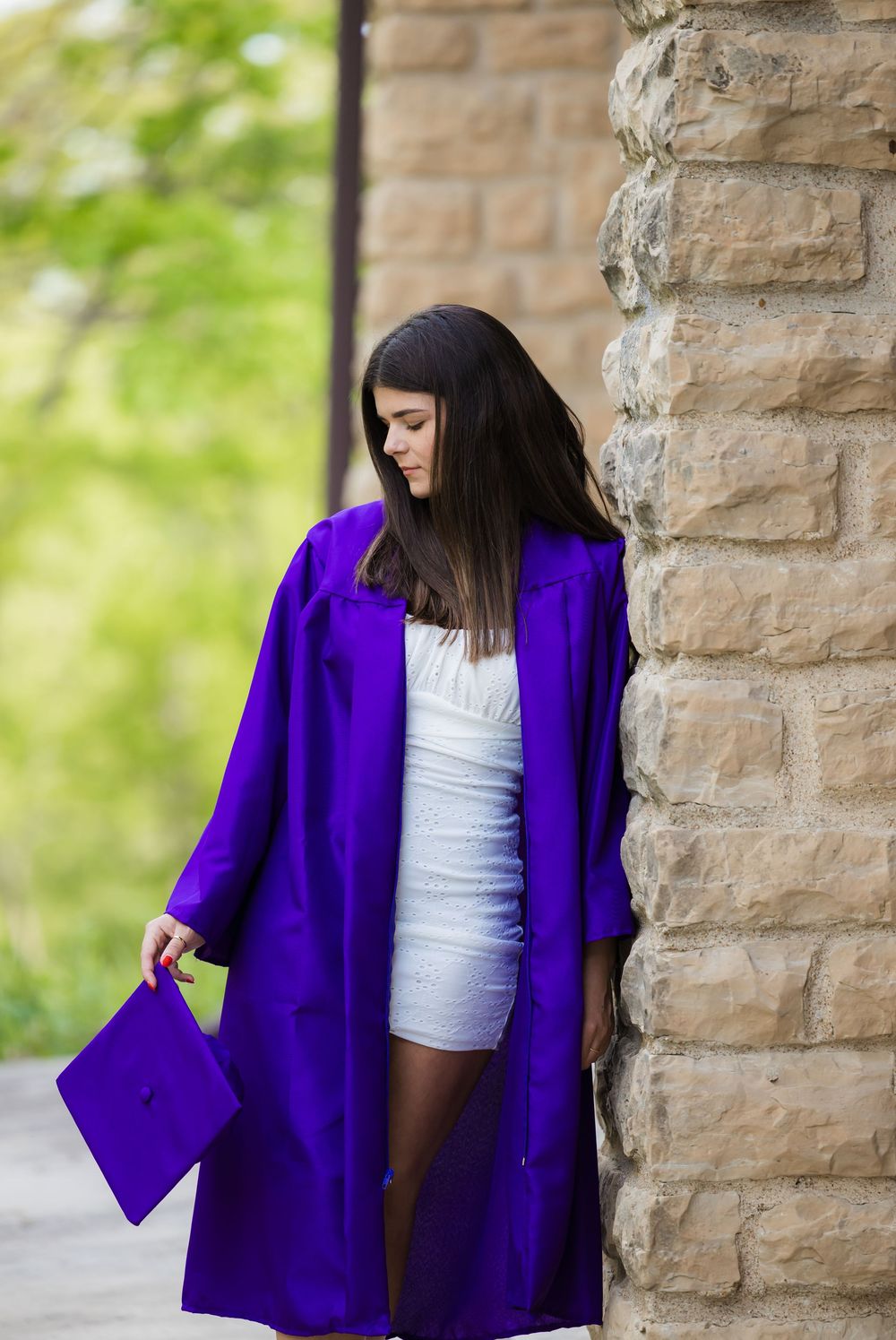 A vibrant purple cardigan is displayed against stone columns and green foliage in an outdoor setting.