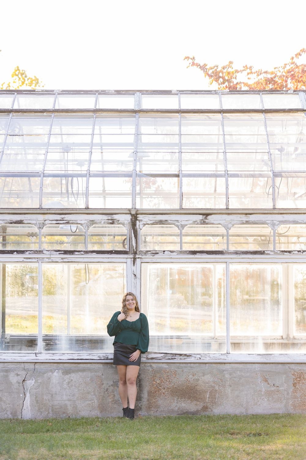 A greenhouse structure with glass panels and concrete base is shown in natural lighting at sunset.