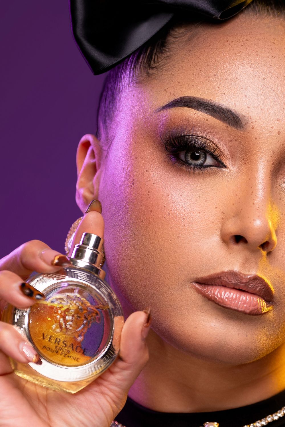 Close-up beauty shot with amber perfume bottle against purple backdrop with dramatic lighting.