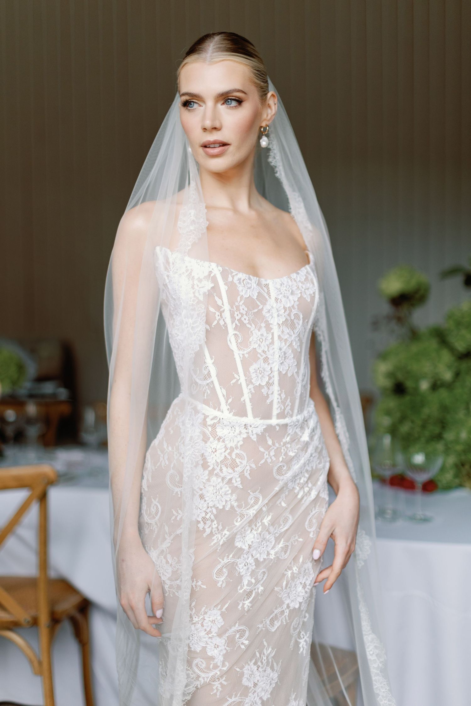 Lace wedding dress with corset bodice and sheer veil in indoor setting.