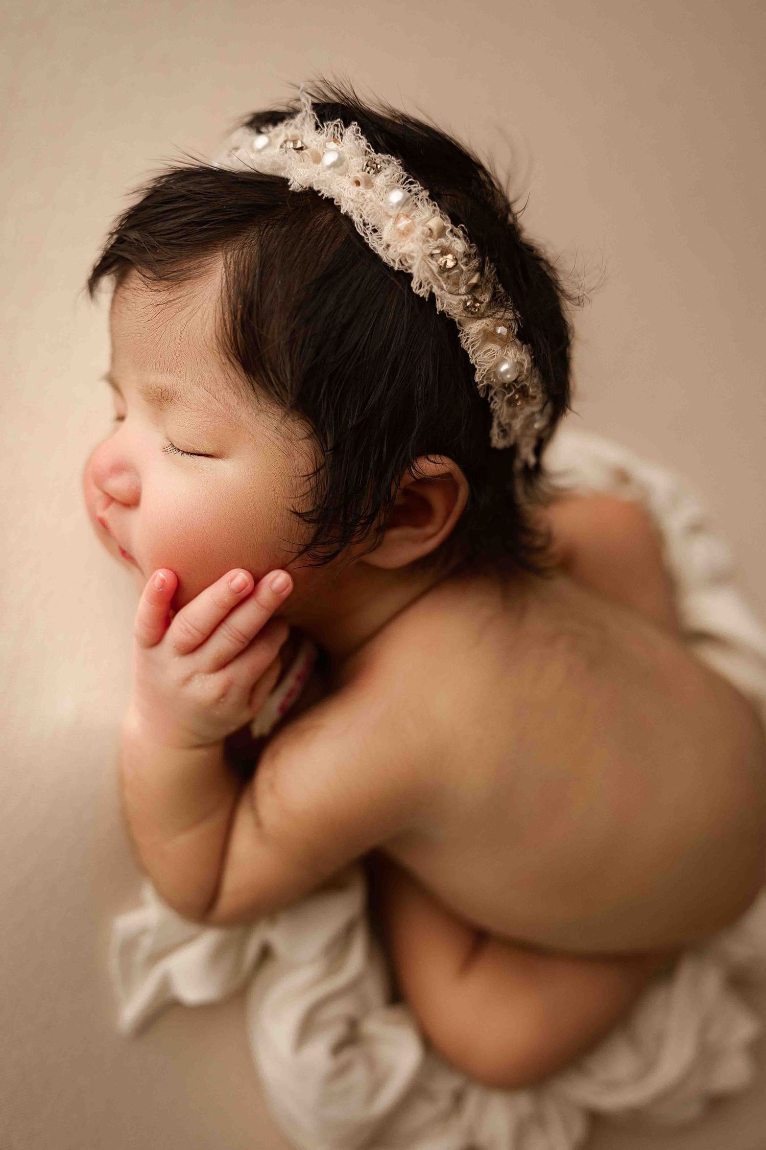 Artistic sequence of five photos showing a sleeping baby wearing a delicate floral headpiece against a soft beige background.