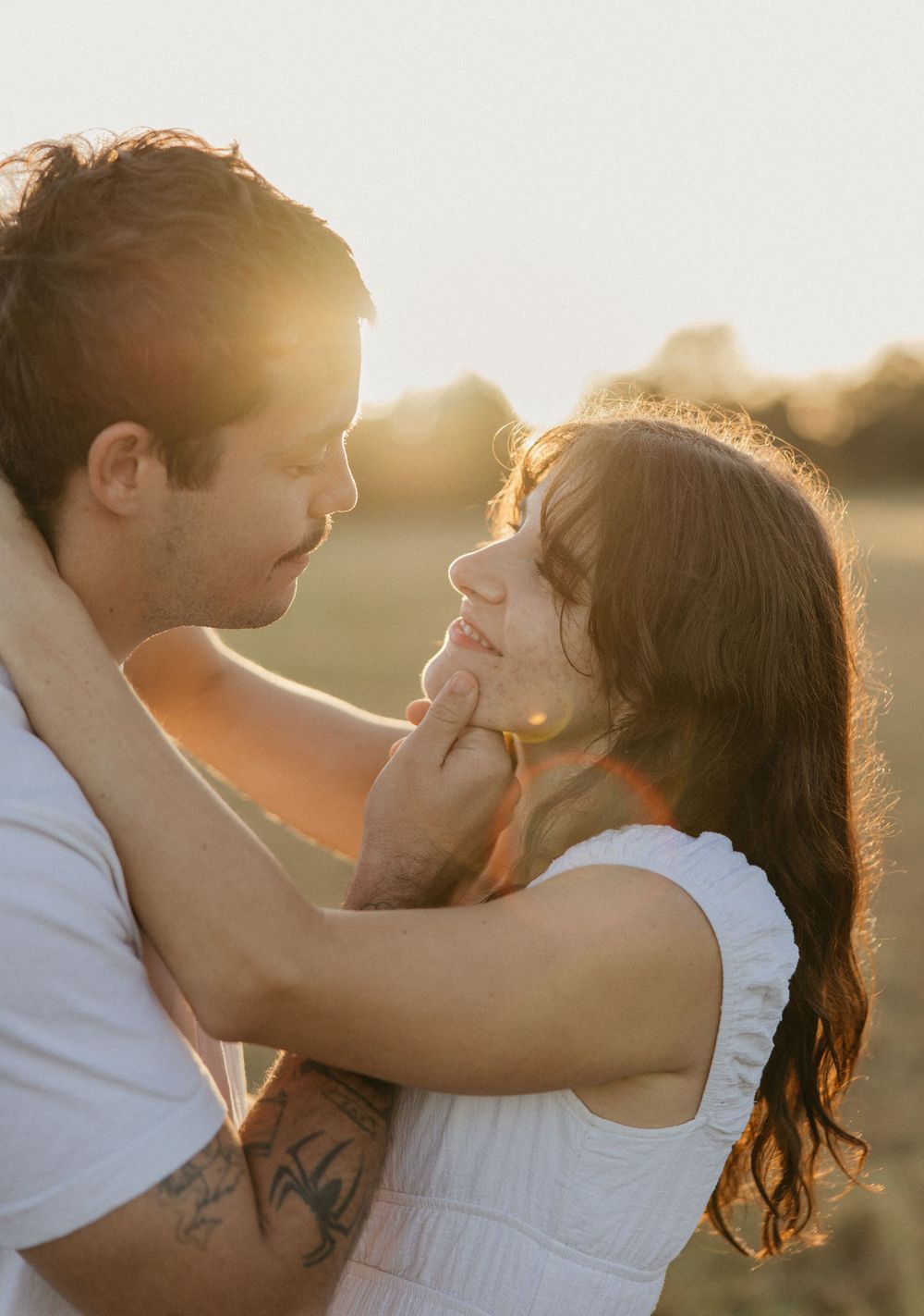 Couple sharing a romantic golden hour moment outdoors, man gently holding woman's face as they gaze at each other.