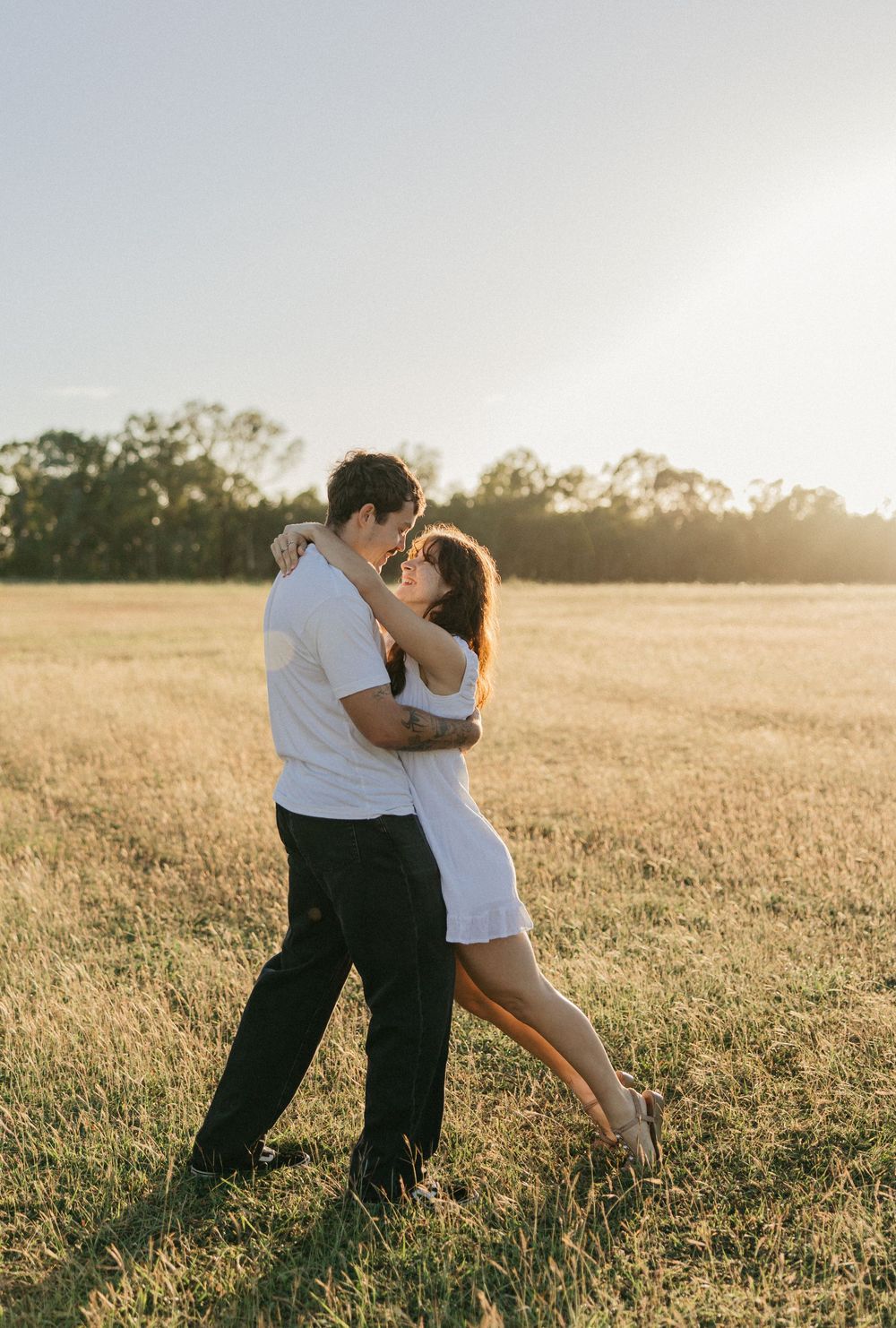 Couple dancing romantically in a golden sunlit field, embracing and leaning in for a kiss at sunset.