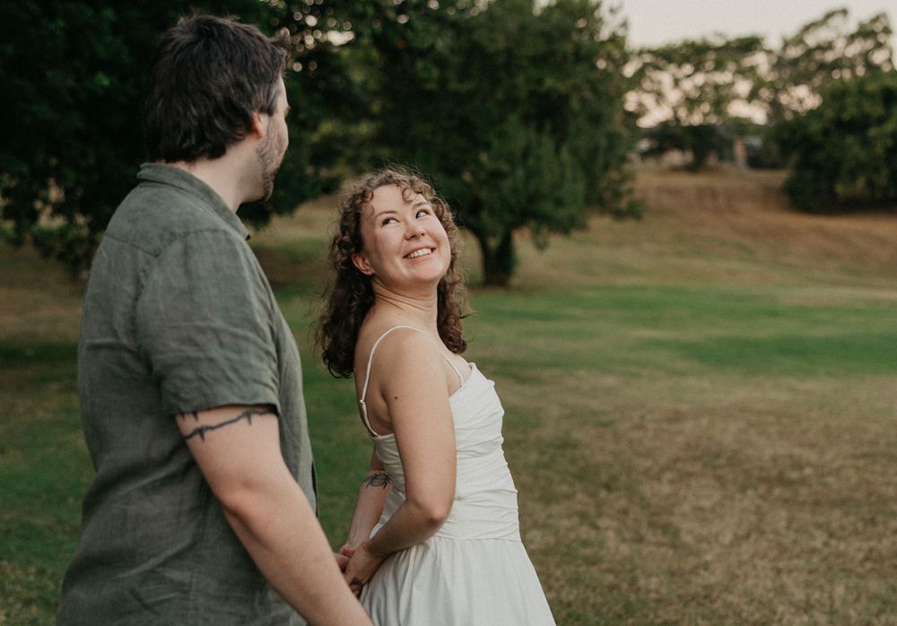 Happy woman in white dress smiles at partner during romantic outdoor couples photography session at golden hour.
