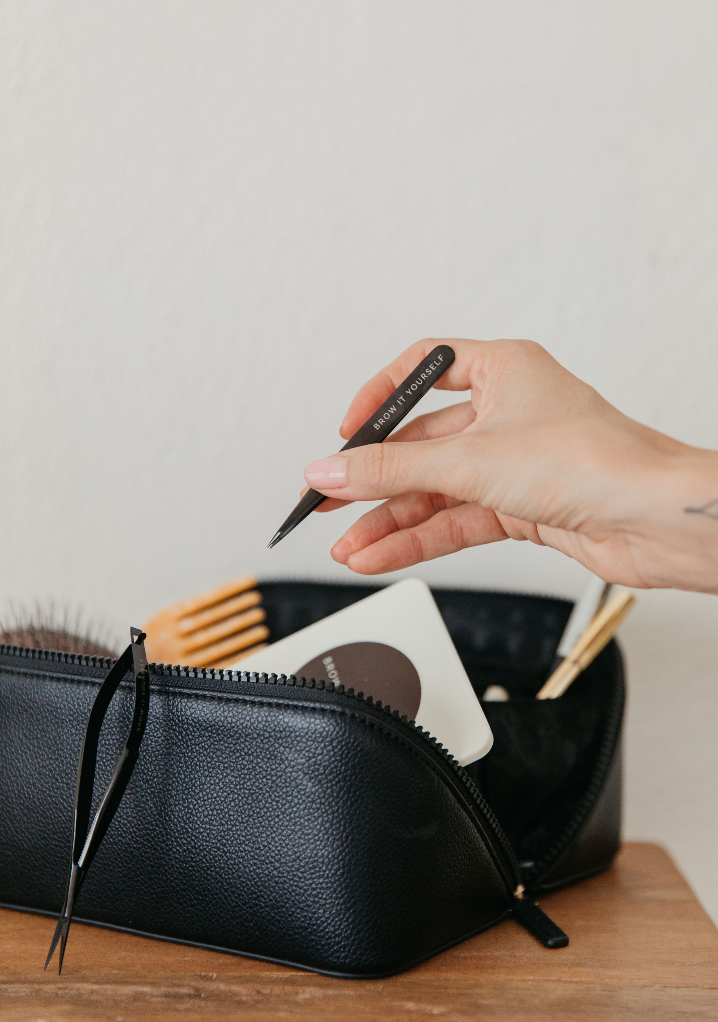 Hand placing a black eyeliner pencil into an open black leather cosmetic bag with beauty tools.
