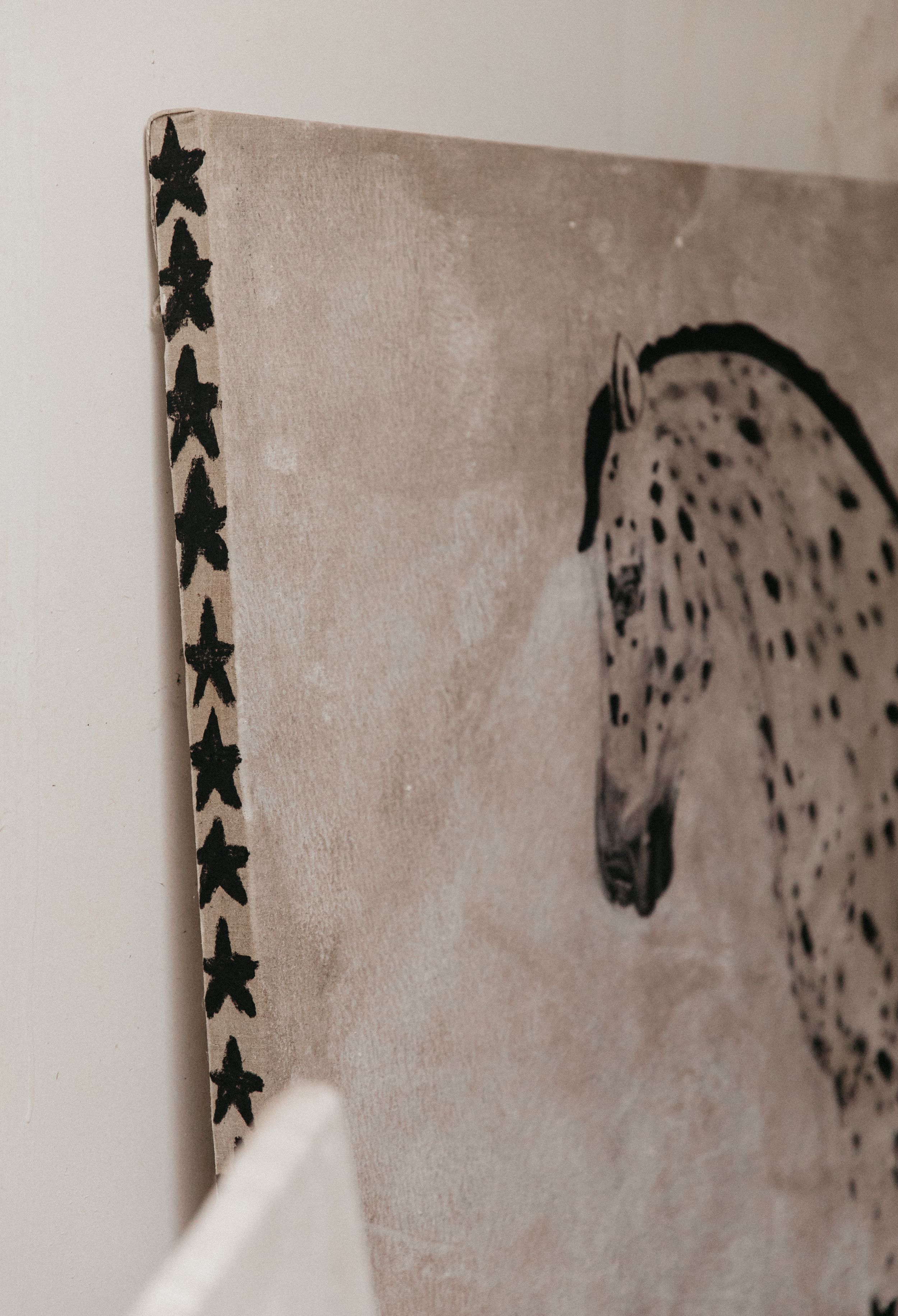 Close-up of a canvas painting featuring a spotted horse with black star border details on a beige background.