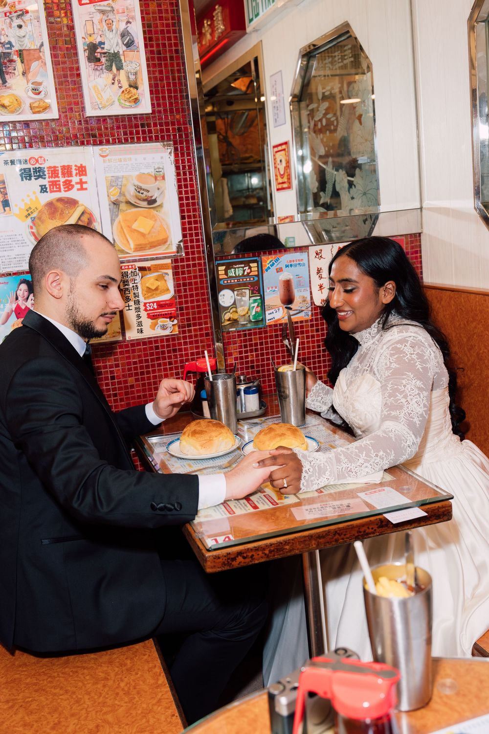A couple shares a meal at a casual Asian restaurant with red tiled walls and menu posters.