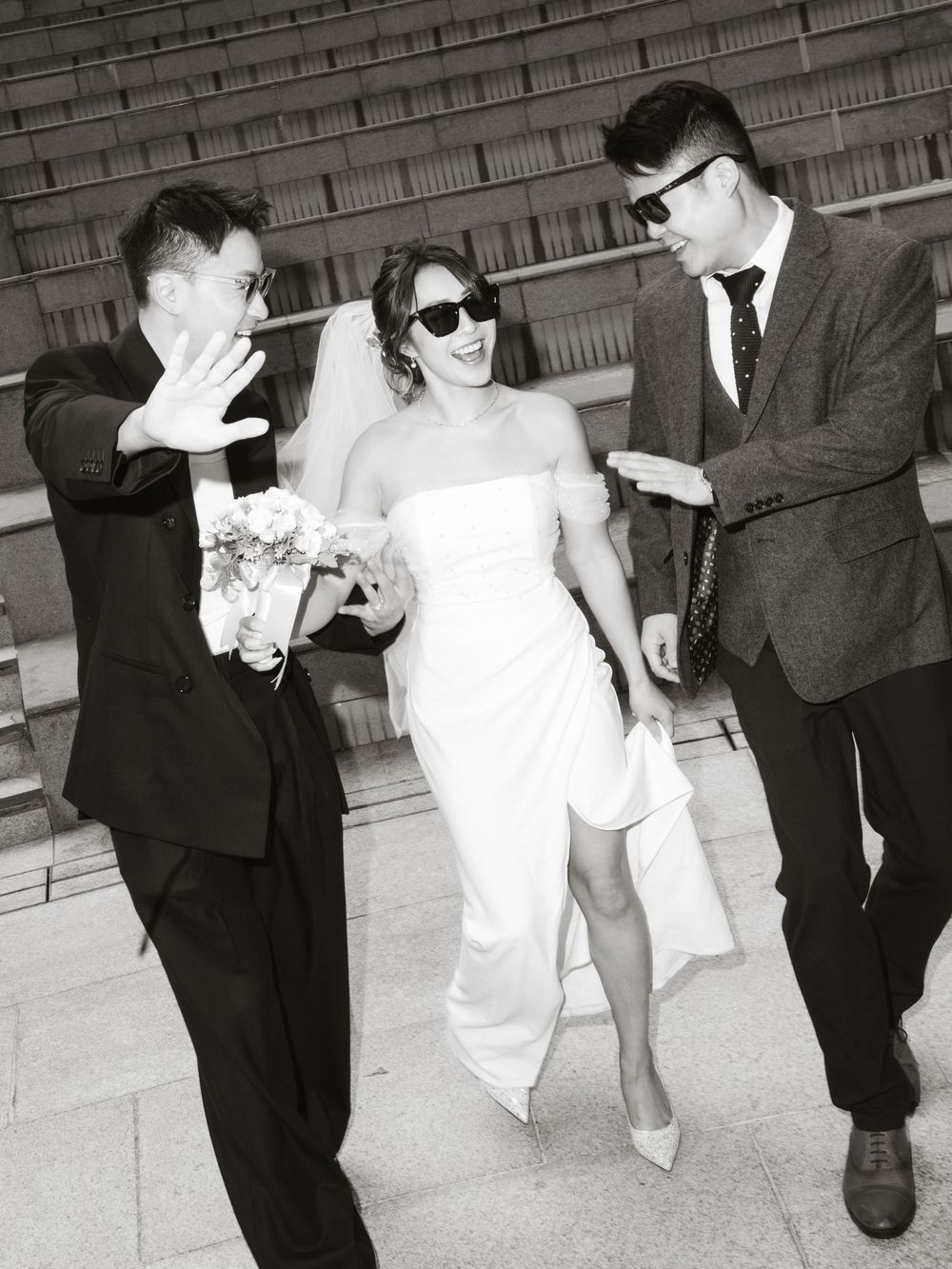 Vintage black and white wedding photo showing playful bridal party walking down steps in sunglasses.