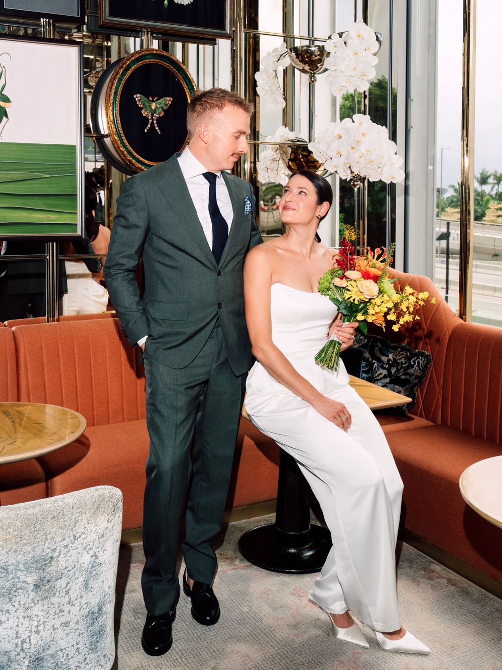Romantic moment in an indoor venue as couple shares intimate glances by large windows in vintage decor setting.