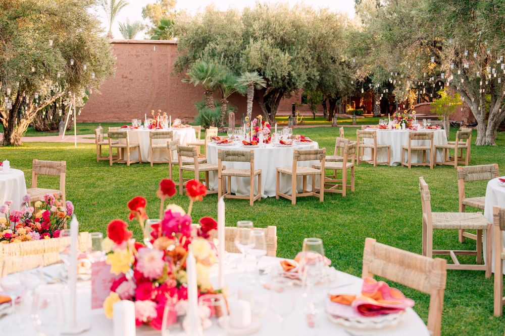 Outdoor wedding reception setup with round tables and colorful floral centerpieces in a garden setting.