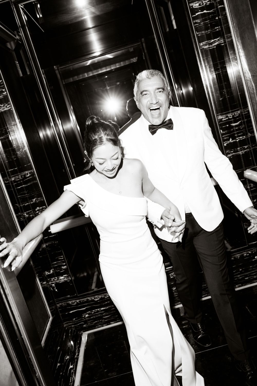 Joyful newlyweds laughing together in formal attire inside elegant hallway at the ritz