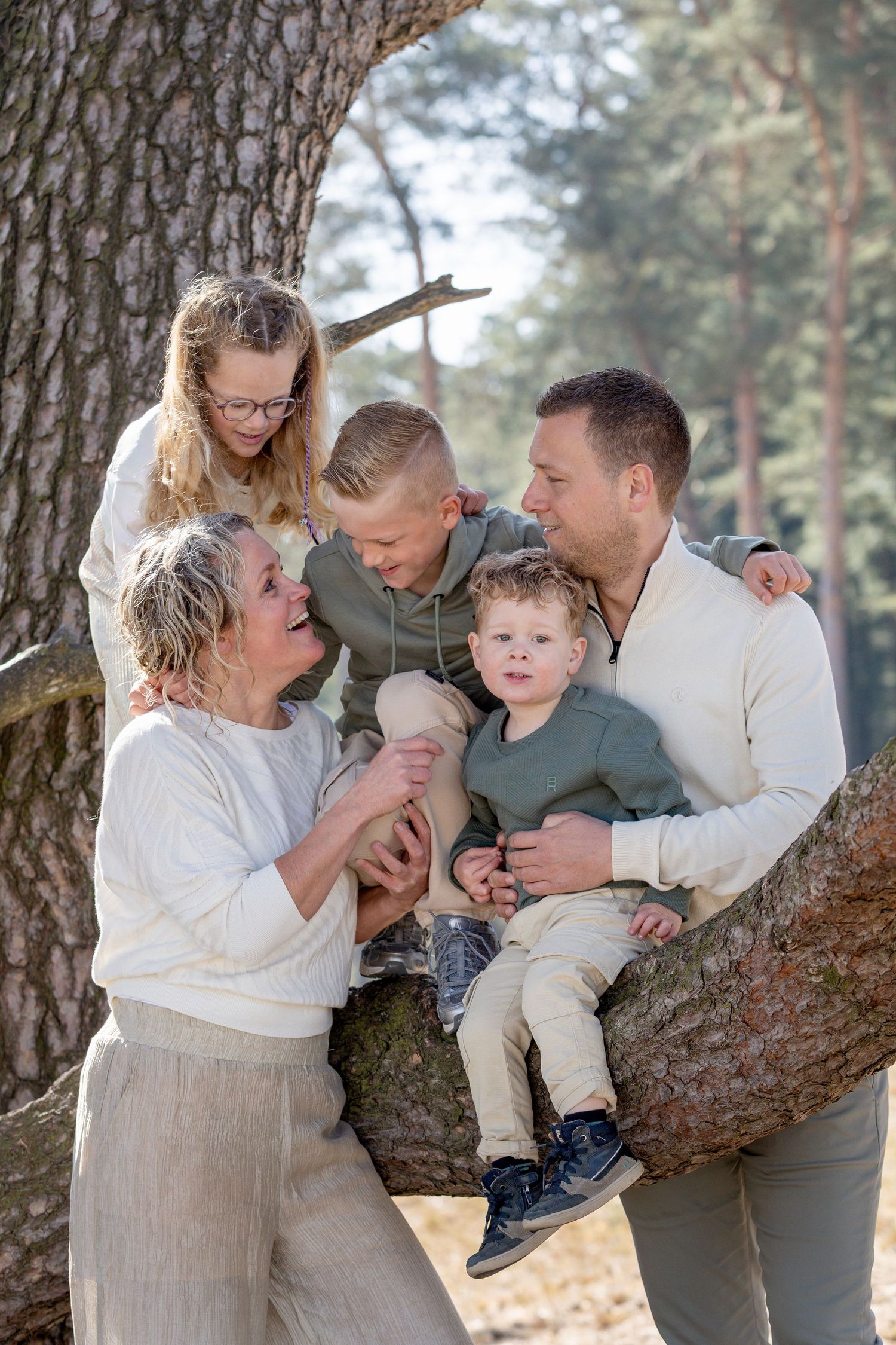 fotograaf lemelerveld. gezin met drie jonge kinderen. kinderen zitten in een boom, ouders staan er naast. ze kietelen elkaar en lachen.