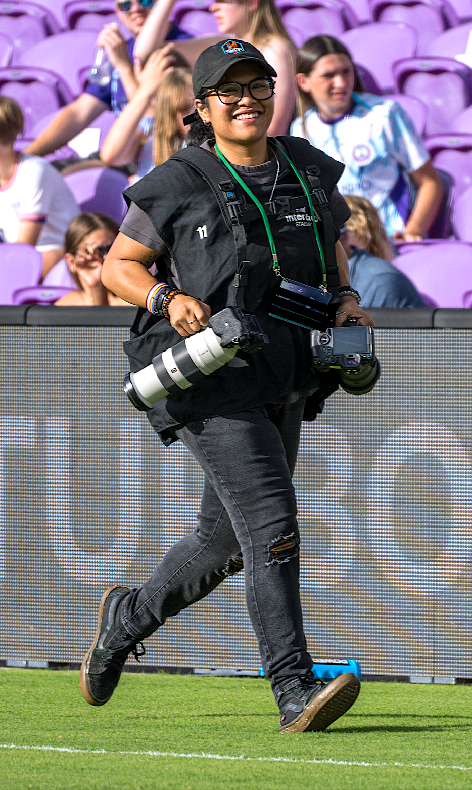 Sports photographers in black attire running with cameras along a stadium sideline.