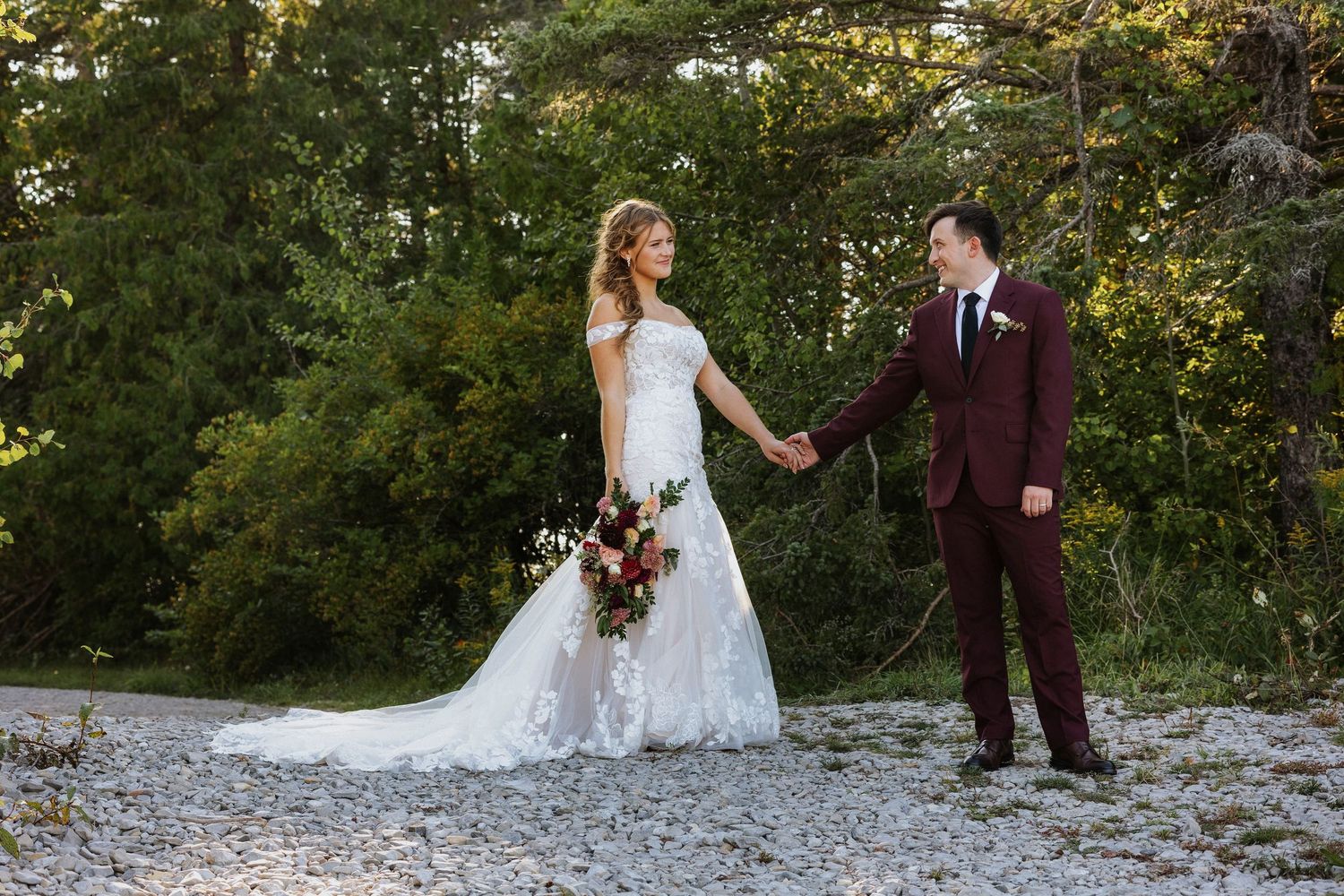 Black and white wedding portrait showing bride in floral dress gazing up lovingly at a groom outdoors by a lake.