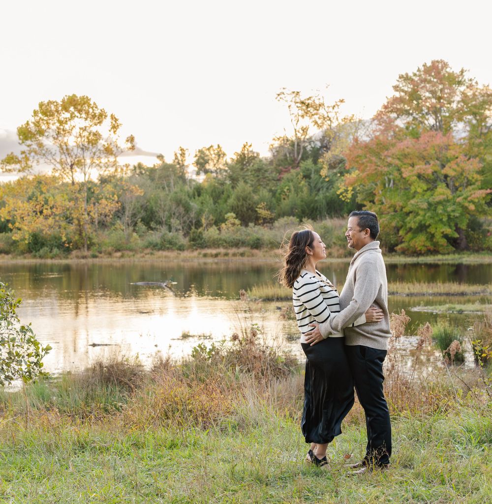 Couple embracing in a beautiful natural setting with autumn trees and a lake.