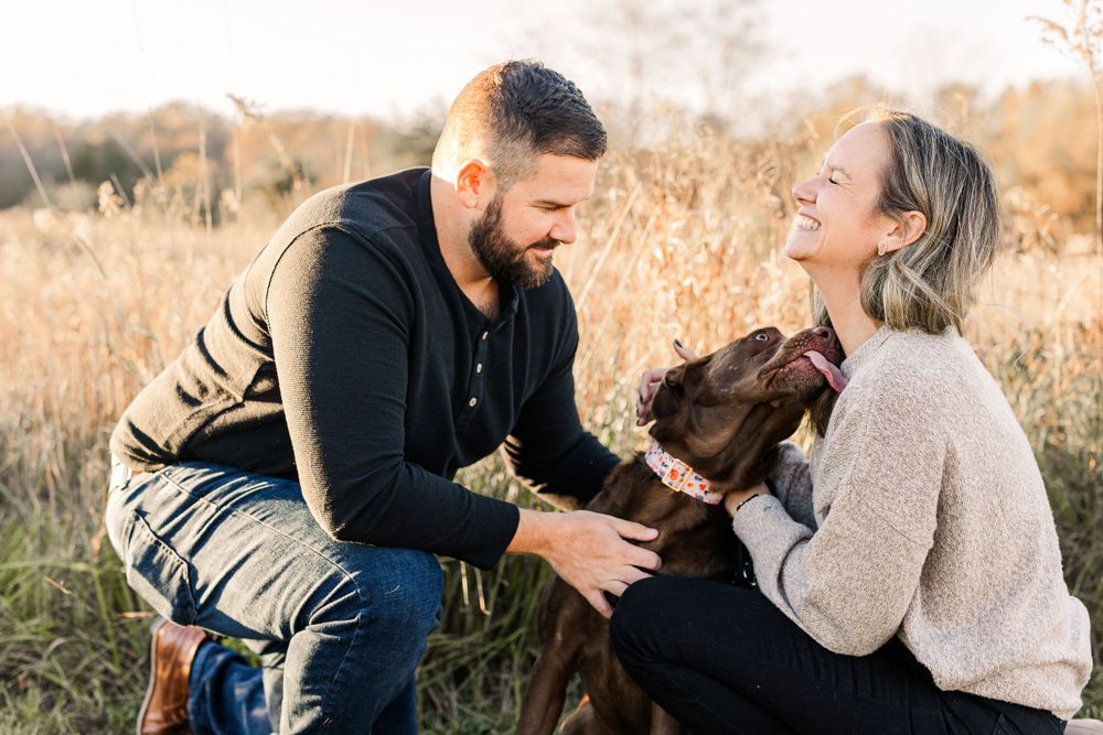 Couple playing with their dog in a golden field during sunset.