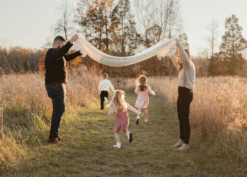 Family playing together with white fabric in autumn field at sunset.