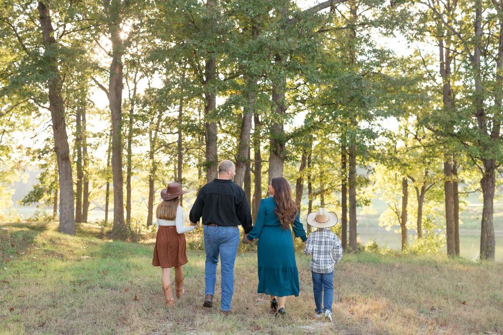 A family holds hands while walking together in a sunlit forest during golden hour.