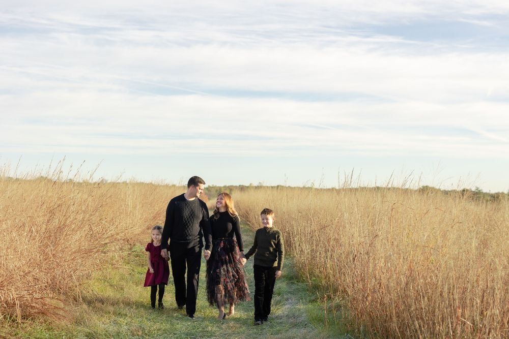A group of people walking through a golden wheat field on a sunny day with blue skies overhead.