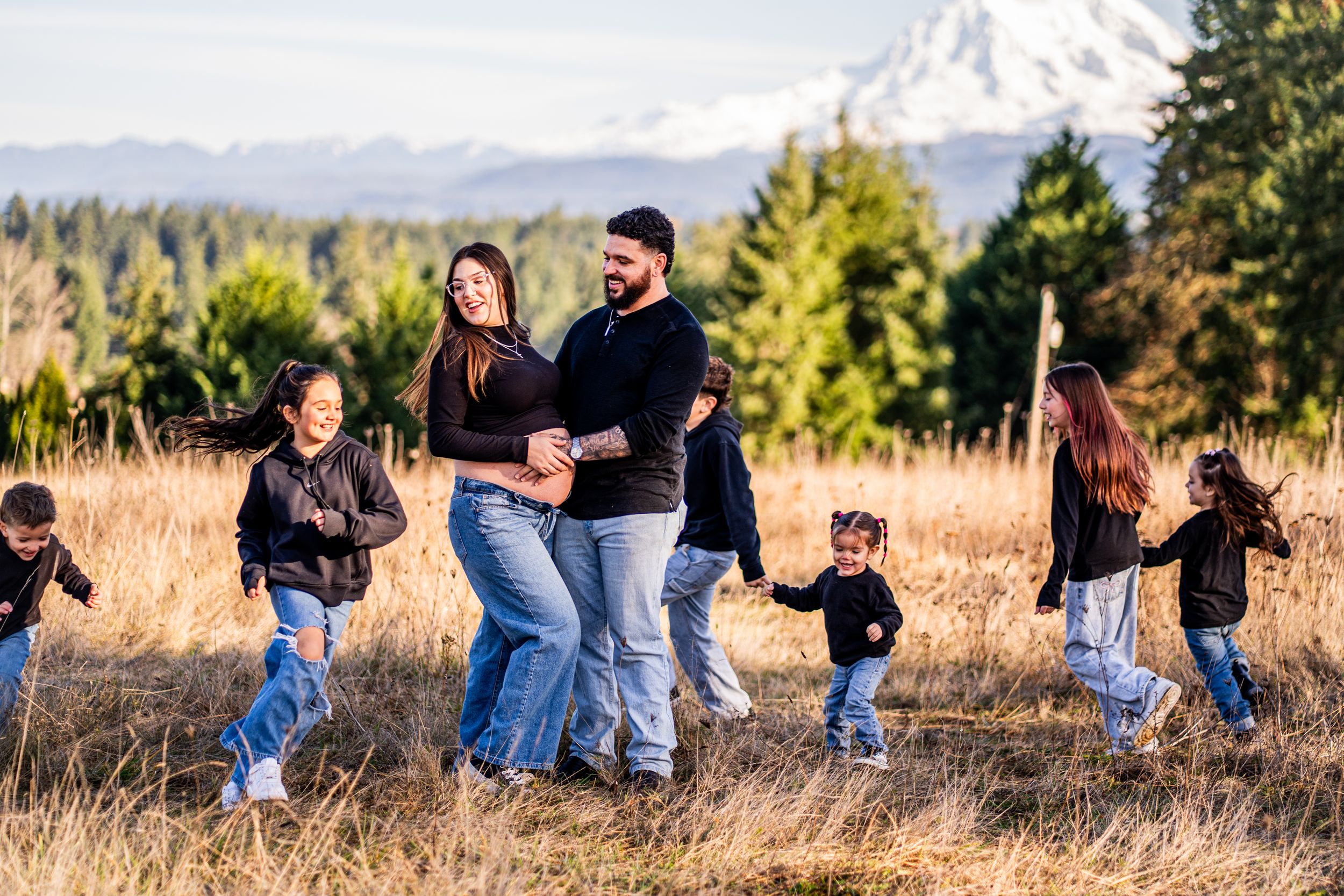 A group of people walk together through a golden field with mountains and evergreen trees in the background.