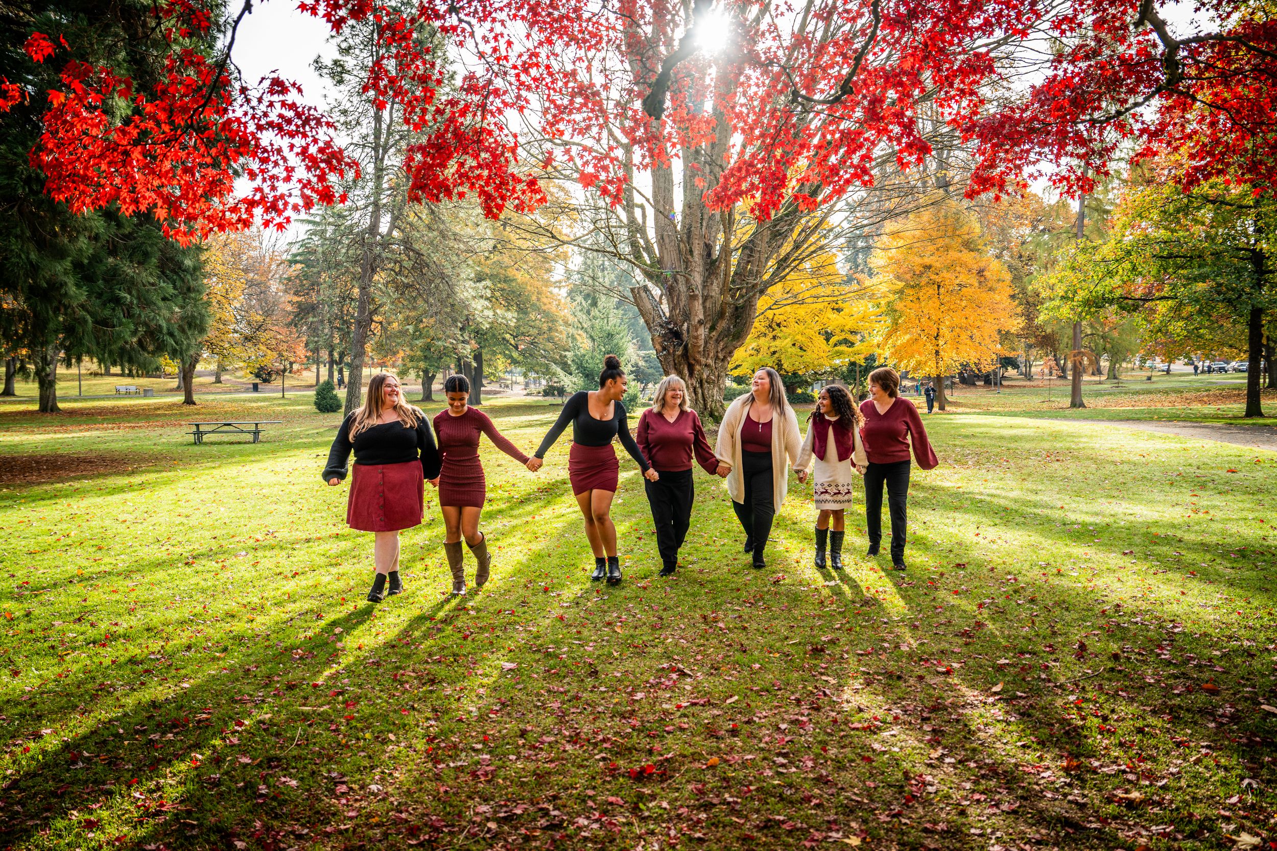Silhouettes of people walking together through a sunlit autumn park with vibrant red and yellow fall foliage.