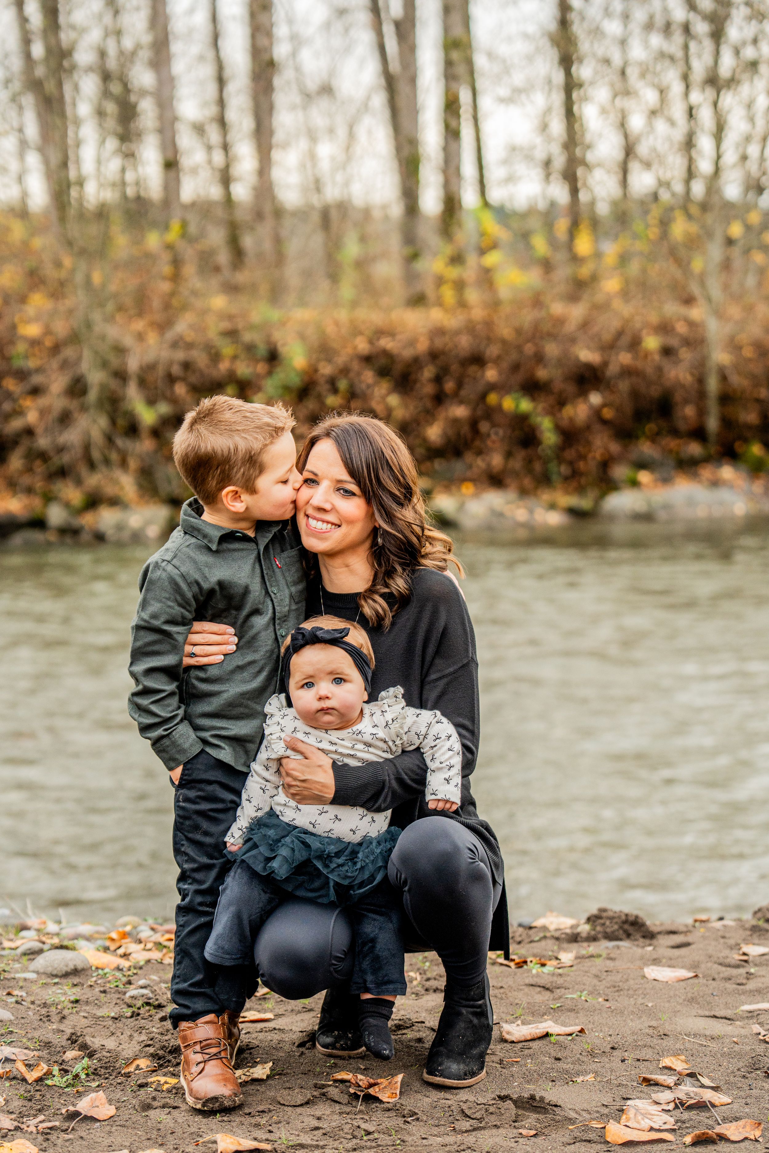 A loving family shares tender moments together by a riverside in autumn with fallen leaves scattered around them.