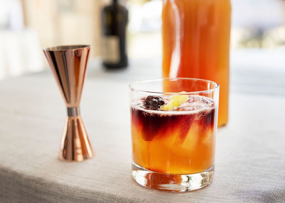 Craft cocktail with orange liquid and dark floater served with copper jigger.