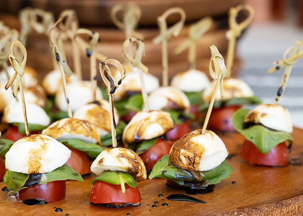 Elegant appetizer bites with mozzarella and basil on skewers arranged in rows.