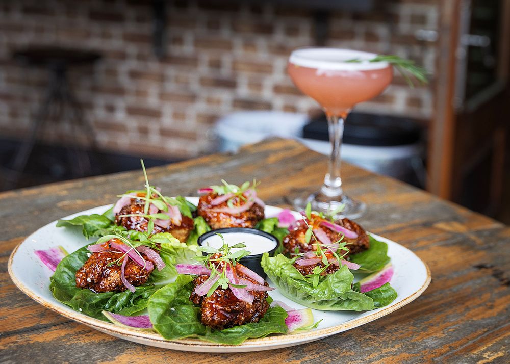 Savory Asian lettuce wraps served with a pink cocktail against a rustic brick wall background.
