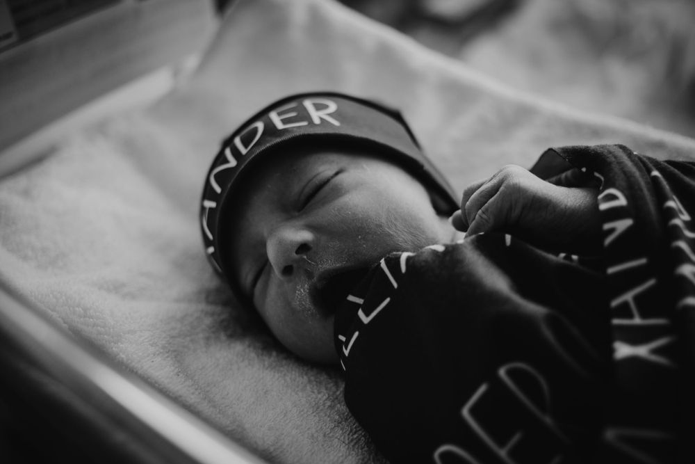 A newborn baby yawning in his hospital bassinet.