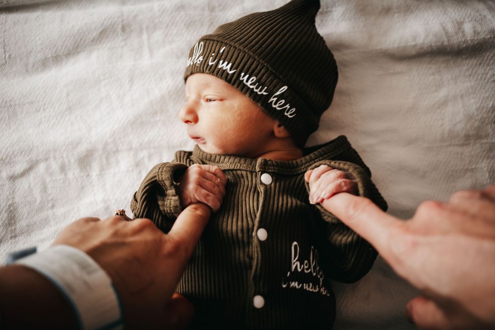 Newborn baby holding his parents fingers.