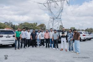 Group of employees gathered for a team photo in front of electrical transmission towers and vehicles.