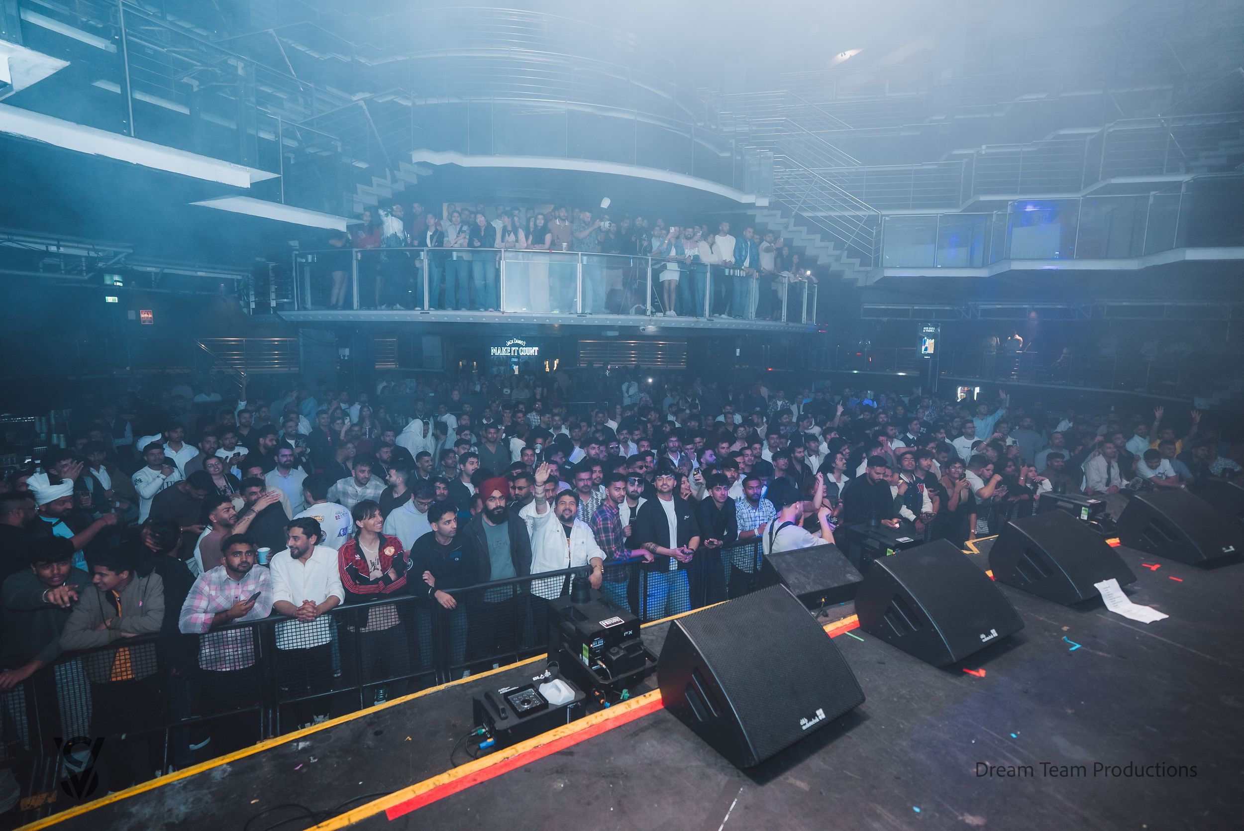 Large crowd of people dancing and enjoying themselves in a dimly lit nightclub with blue lighting effects.